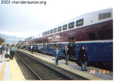 From 2001: ACE train arriving at Santa Clara Train Station. Double-decker train has a white roof, with large purple and blue stripes, separated by a small white stripe,