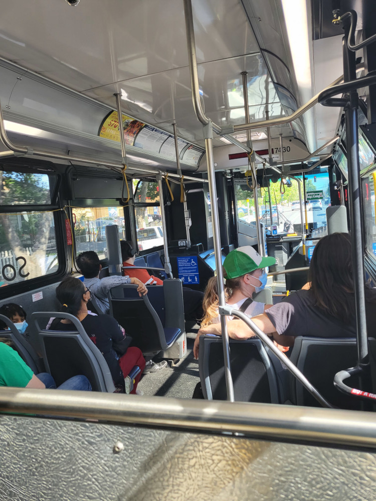 Several people are seated aboard a VTA bus moving within the City of San Jose. Seats have grey backs. Camera faces front of bus.